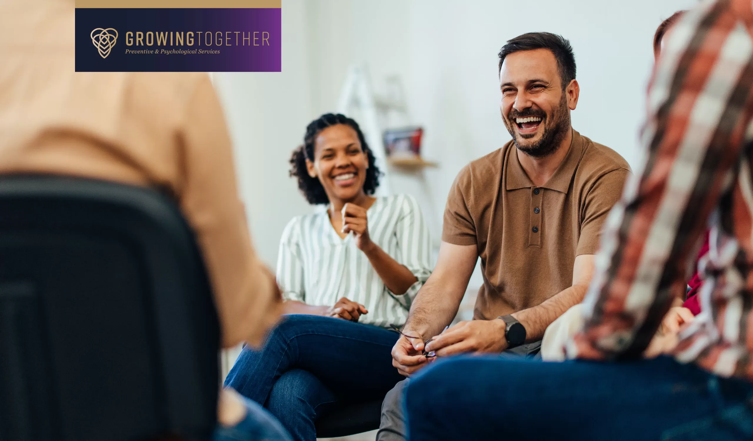 Adult men and women sit in a circle for group therapy while smiling and laughing.