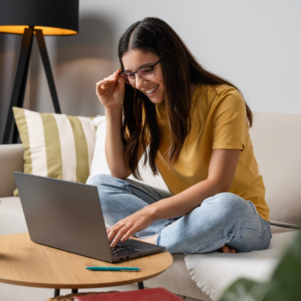 A young woman wearing glasses smiling while looking at her laptop.