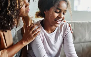 A young girl and her mother sit in children's therapy with a licensed therapist.