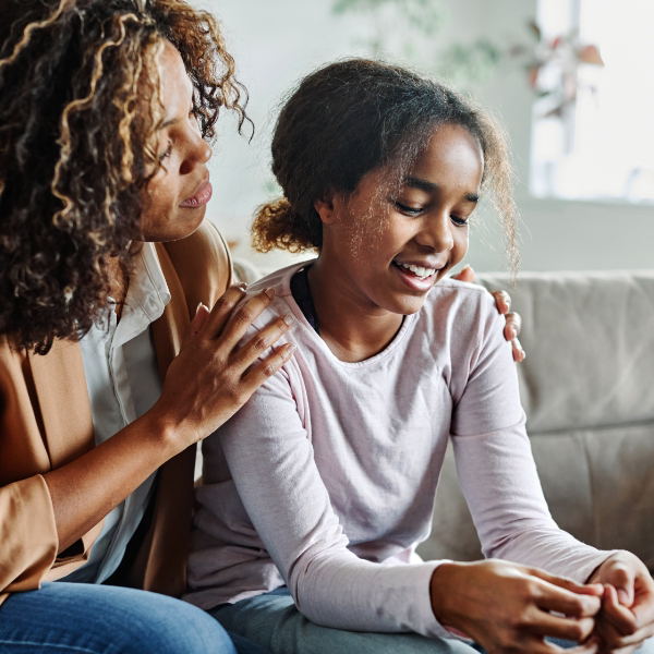 A young girl and her mother sit in children's therapy with a licensed therapist.