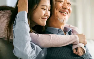 An older man hugs his teenage daughter in their home.