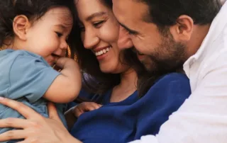 A man and woman hold their young child and smile.