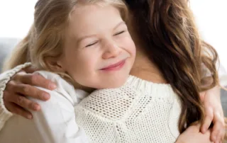 A young girl hugs her mother while smiling.