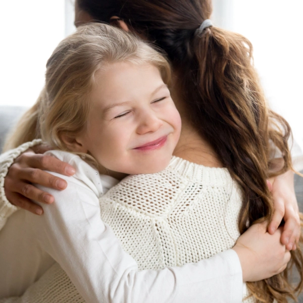 A young girl hugs her mother while smiling.