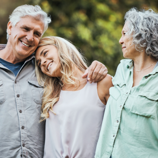An older couple hugs their teenage daughter while outside.
