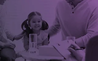 A young girl sits with her parents while talking to a dyadic therapist.