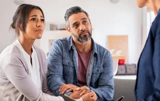 A middle-aged couple looks at their therapist while she talks.
