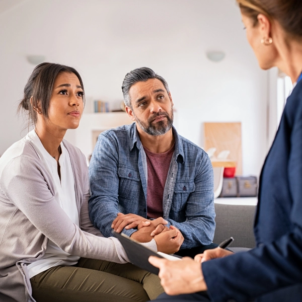 A middle-aged couple looks at their therapist while she talks.