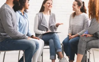5 young adults sit in a circle while in group therapy.