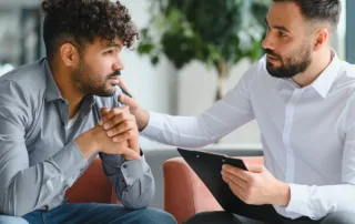 A professional therapist talks to a young man in therapy.