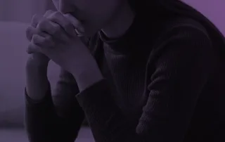 A woman rests her face on her folded hands.