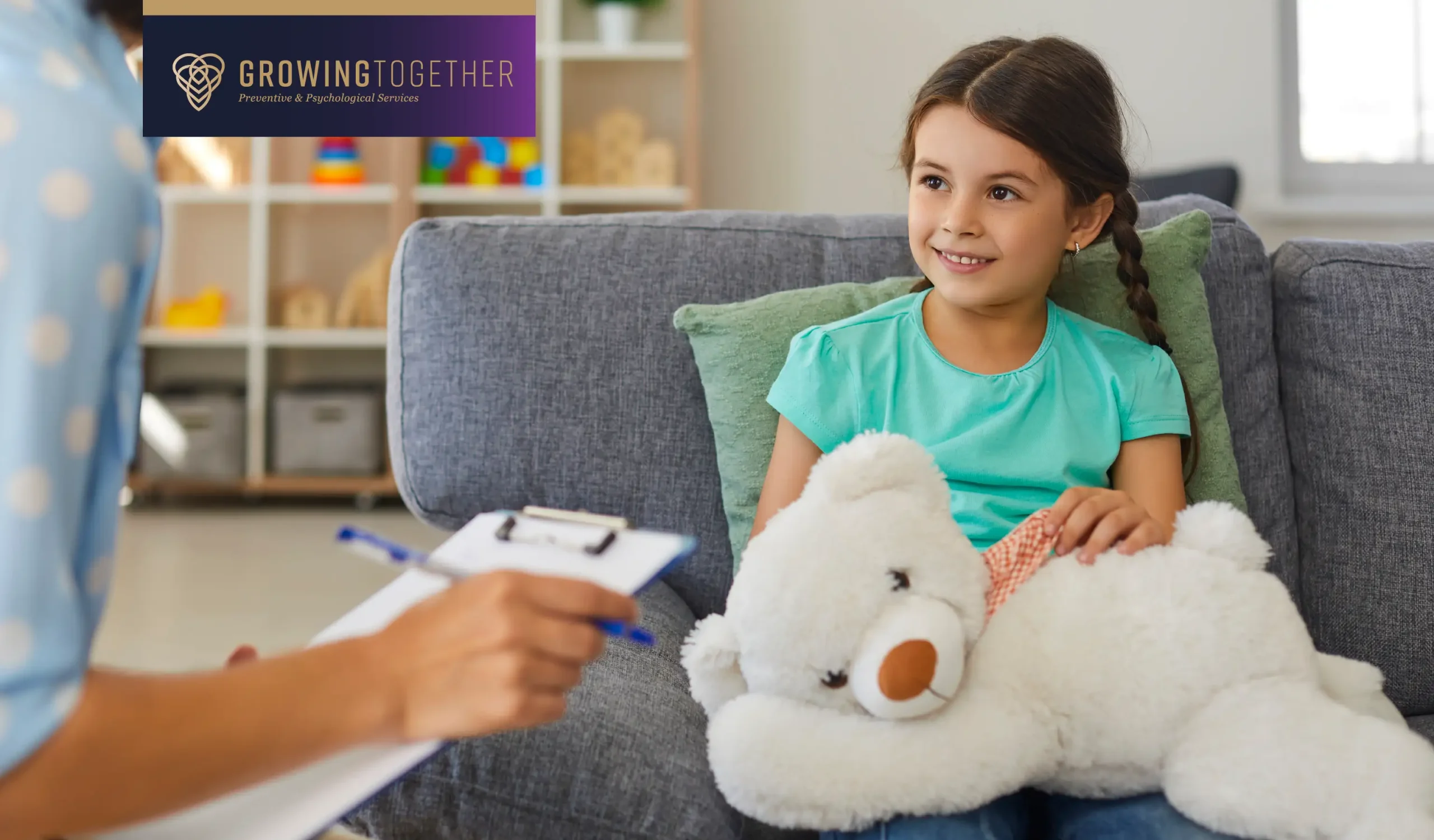 Little smiling girl with stuffed animal talking to child psychologist during therapy session in office.